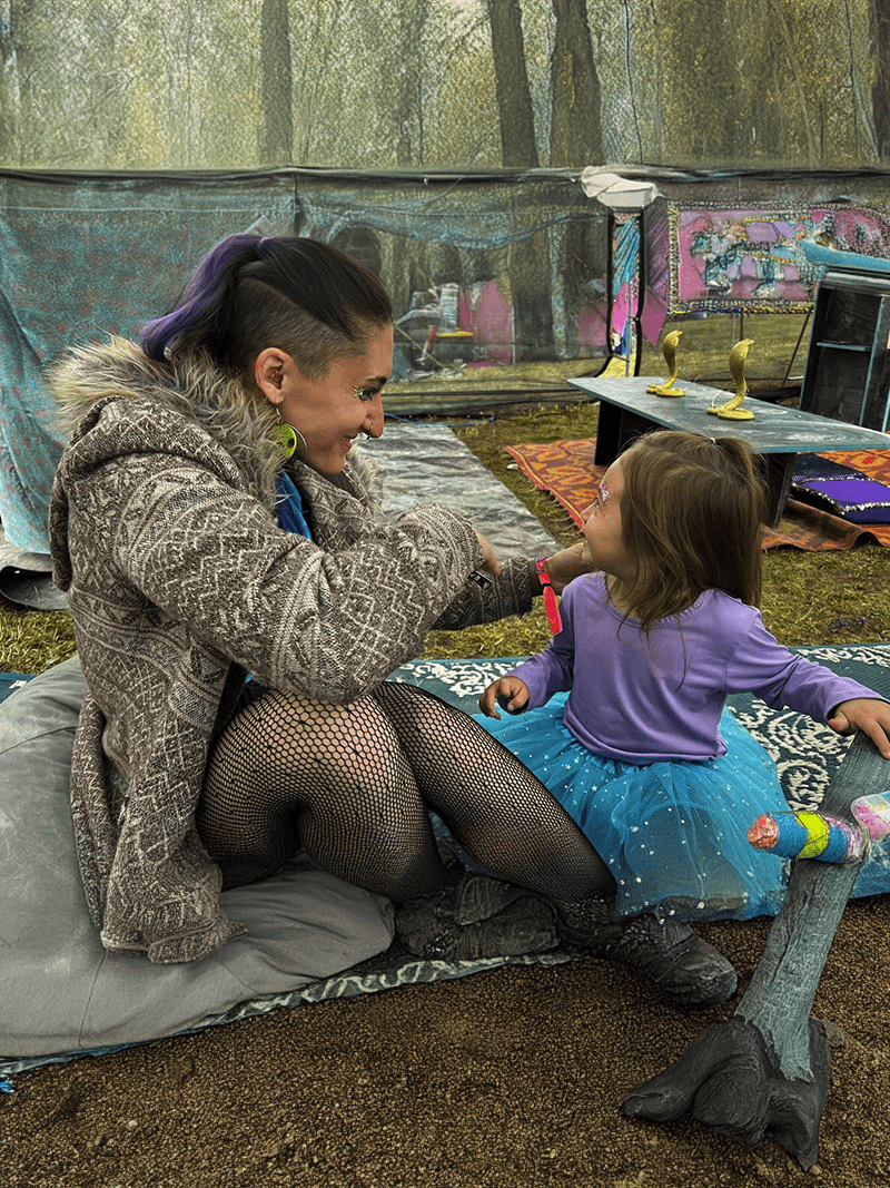 Festival nanny helping child with face paint in cozy outdoor lounge area
