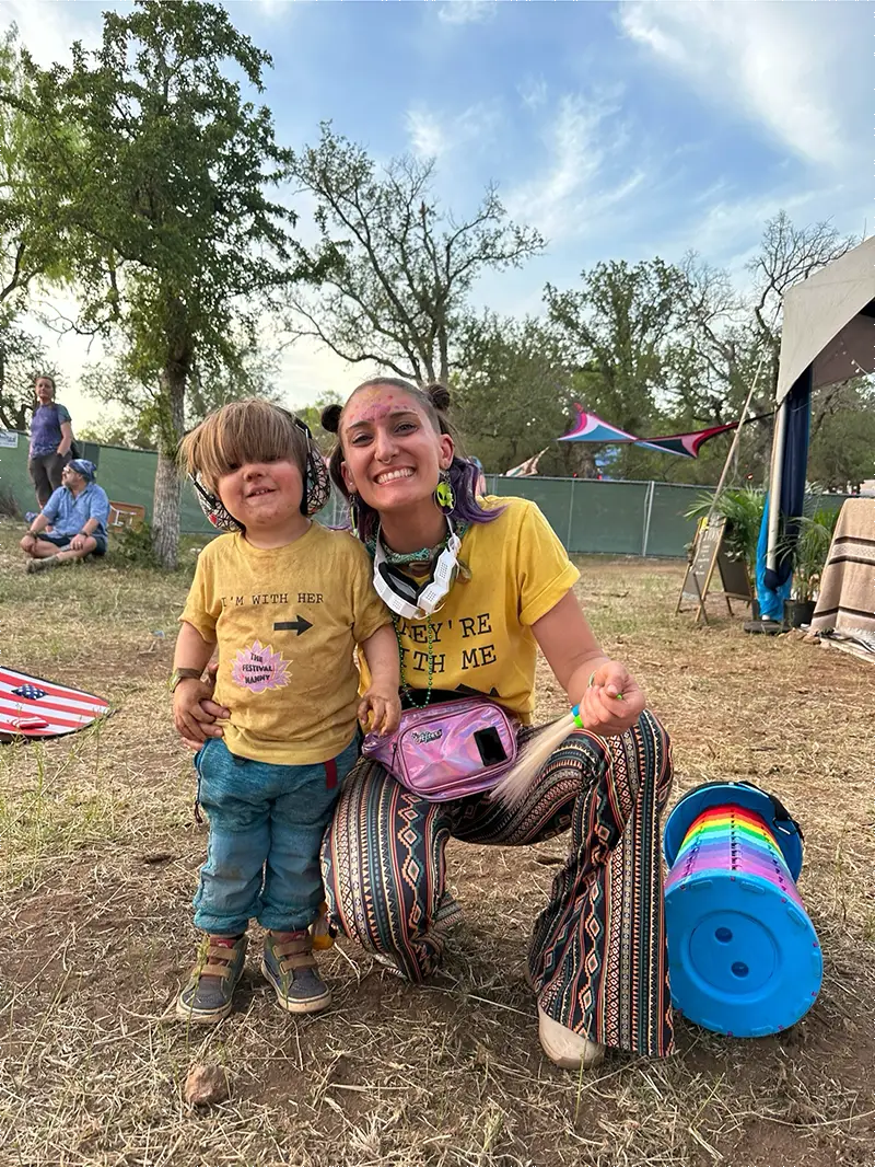 Festival nanny and child wearing matching shirts and ear protection at outdoor music festival